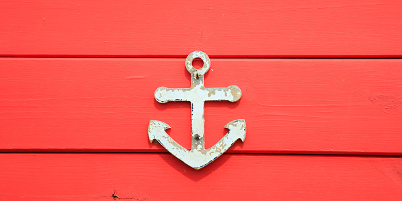 Anchor symbol on aged surface. Peeled sign, red blank board background, close up view.