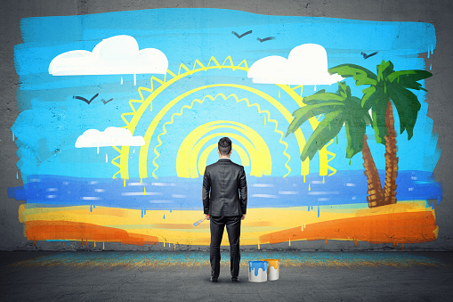 A businessman stands with his back turned and looking at a finished wall picture of exotic isle. Business and leisure. Work and vacation. Dreaming of getting away.