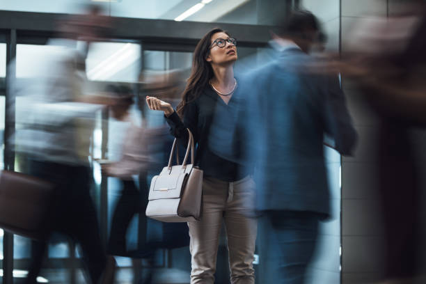 Woman waiting during rush hour in lobby Businesswoman standing and looking upwards while waiting for someone with people rushing in the lobby. Motion blur effect. hotel reception hotel business lobby stock pictures, royalty-free photos & images