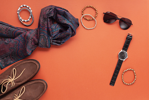 Flat lay of men's accessories with shoes, watch, phone, earphones, sunglasses, scarf over the orange background. Sales, Shopping, gift ideas. Top view