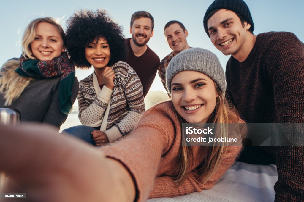 Friends taking selfie during beach party Young friends taking selfie during beach party. Group of mixed race  friends taking selfie on the seashore. Friendship Stock Photo