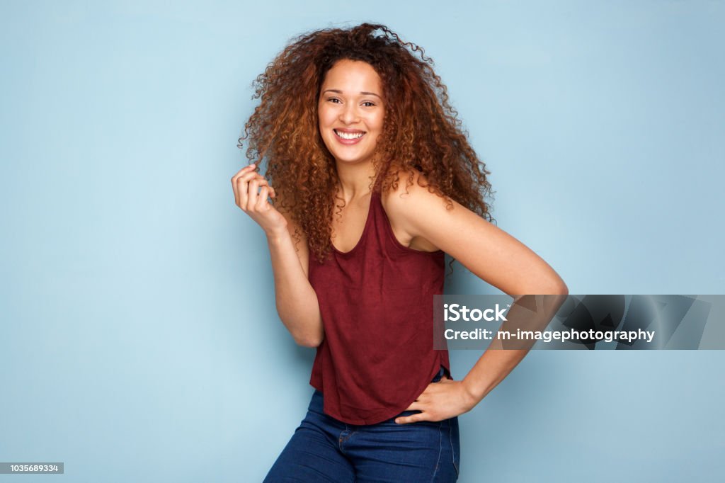 cheerful young woman with curly hair smiling against blue background Portrait of cheerful young woman with curly hair smiling against blue background One Woman Only Stock Photo