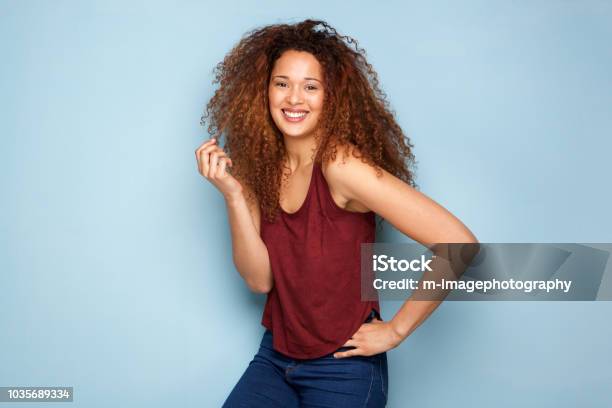 Cheerful Young Woman With Curly Hair Smiling Against Blue Background Stock Photo - Download Image Now