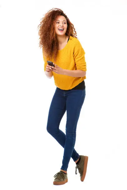 Full body portrait of happy woman with cellphone laughing against isolated white background