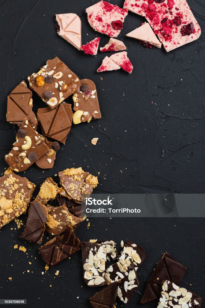 Luxury handmade chocolate on black background Crashed handcrafted chocolate with nuts, cookie, biscuit crumb, raspberry toppings on black background. Top view Chocolate Stock Photo