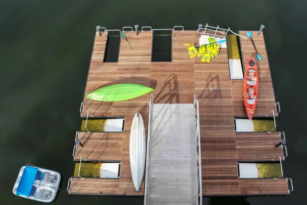 Top view of wooden pier with launchers - kayaks and paddles and life vests scattered around and a paddleboat in the water