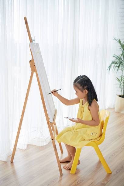 Little Vietnamese girl painiting on easel in her room