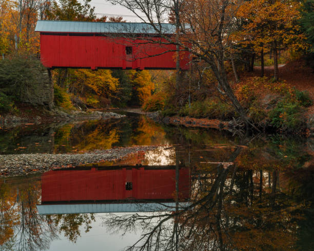 istock Red covered bridge with reflection over a tranquil stream with autumn colors 1035724602