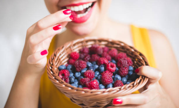 Woman eating fresh fruits The young woman smiles while holding and eating from a basket filled with raspberries and blueberries berry stock pictures, royalty-free photos & images