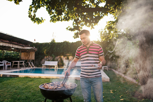 A mid adult man is cooking meat on bbq