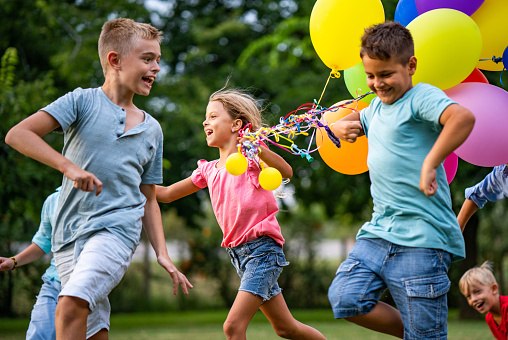 Group of children running with balloons in nature celebrating birthday