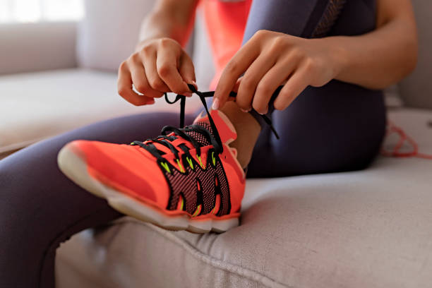 Get ready to run your own life Young Woman Sitting in Living Room and Tying Shoelaces on Sneakers and Getting Ready for Fitness. Healthy Lifestyle Concept bound woman stock pictures, royalty-free photos & images