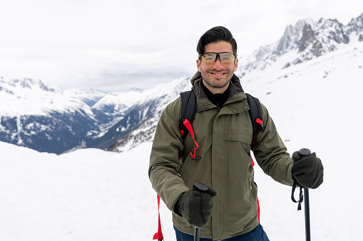 Portrait of a happy Latin American man trekking in snow mountains using poles and looking at the camera smiling