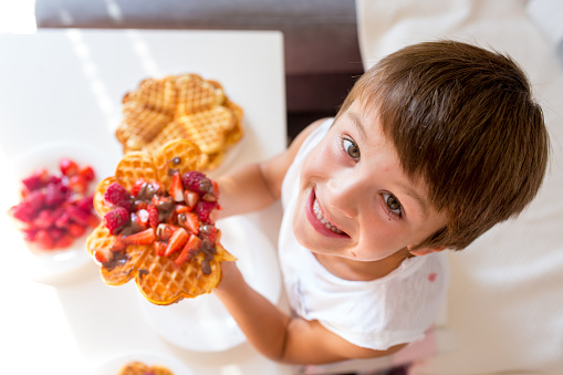 Sweet birthday boy, eating Belgian waffle with strawberries, raspberries and chocolate at home