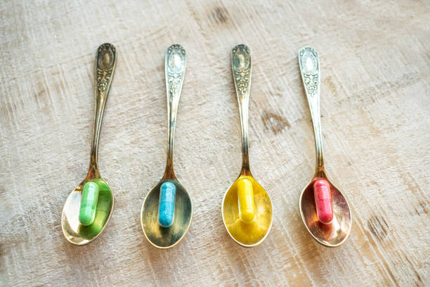 istock 4 four multi-colored capsules (yellow, red, blue and green) in 4 vintage metal spoons on a wooden background. Different pills and drugs tablets. Pharmacy antibiotic antidepressant. 1035786300