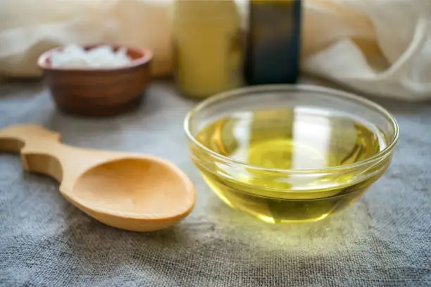 Photo of Liquid coconut MCT oil in round glass bowl with wooden spoon and bottles. Health Benefits of MCT Oil. Triglycerides, a form of saturated fatty acid.