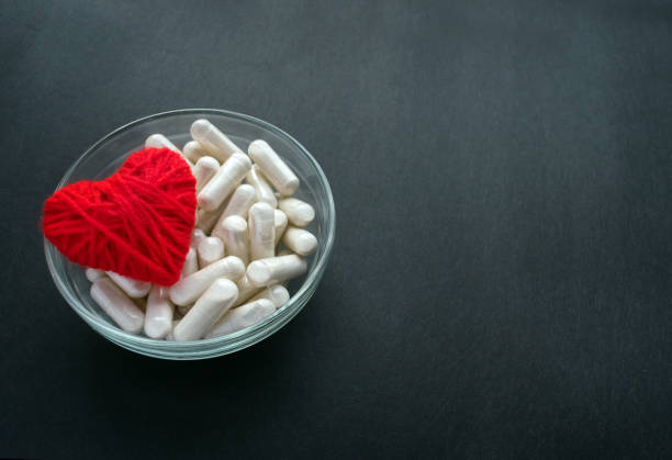 White veg capsules and red thread heart in glass bowl on black background. Anticoagulant, Blood Thinners. Cardiac Medications, pills for the heart. Treat Heart disease Failure White veg capsules and red thread heart in glass bowl on black background. Anticoagulant, Blood Thinners. Cardiac Medications, pills for the heart. Treat Heart disease Failure blood thinners stock pictures, royalty-free photos & images