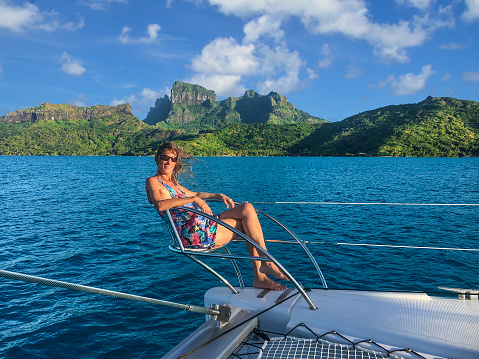 Happy woman in one on the bow seats on a catamaran. Bora Bora lagoon, French Polynesia. South Pacific Ocean.