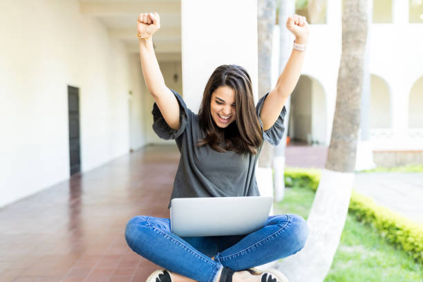 fêmea com braços levantados gritando enquanto estiver usando o laptop na grade - cheering arms raised women university - fotografias e filmes do acervo