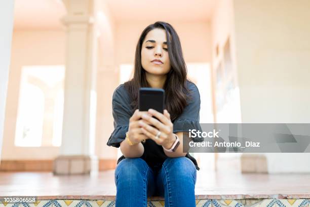 Woman Checking Email On Modern Cellular While Sitting At Corridor Stock Photo - Download Image Now