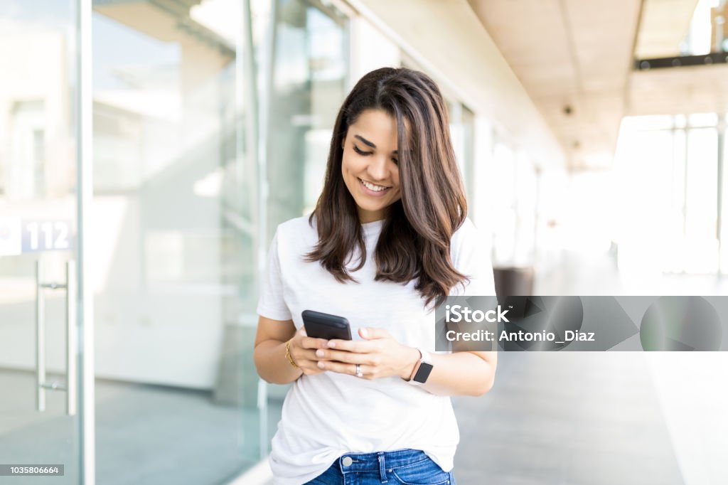 Woman Reading Incoming Notification On Smartphone Happy mid adult woman reading incoming notification on smartphone in shopping mall Banking Stock Photo