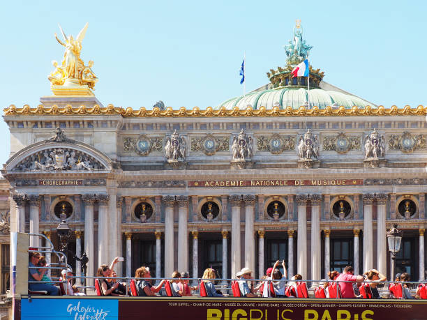 Group of tourists in an open tourist bus on the background of the facade of the Palais Garnier opera house. National Academy of Music. Square Place de l'Opera Paris, France - June, 2018: Group of tourists in an open tourist bus on the background of the facade of the Palais Garnier opera house. National Academy of Music. Square Place de l'Opera place de lopera stock pictures, royalty-free photos & images