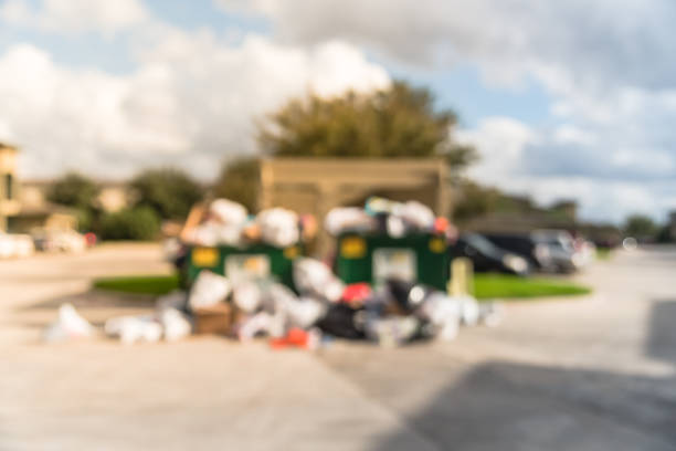 Blurred an overflowing dumpster at apartment building yard in Humble, Texas, US. Overfilled and on ground full of household waste, plastic bag, mattress, boxes after holidays. Urban garbage management