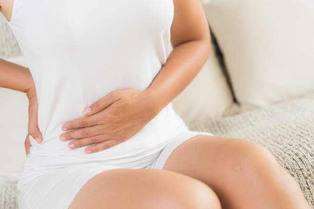 Young woman having painful stomachache and back pain sitting on sofa at home. Chronic gastritis. Abdomen bloating concept. Young woman having painful stomachache and back pain sitting on sofa at home. Chronic gastritis. Abdomen bloating concept. endometriosis bloated stock pictures, royalty-free photos & images