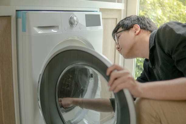 istock Young Asian technician looking into washing machine checking inside. Appliance maintenance in laundry at home. Techonology concept 1035889714