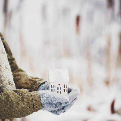 Female hands holding tiny house in snowy weather