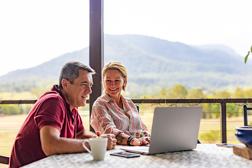 Mature couple using a laptop computer on the verandah of their farm in rural Australia