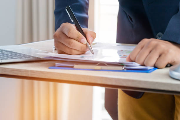 istock Document Report and business busy Concept: Businessman Manager checking and signing documents reports papers with calculator, laptop computer on stacks of paper files in modern office. 1035938476