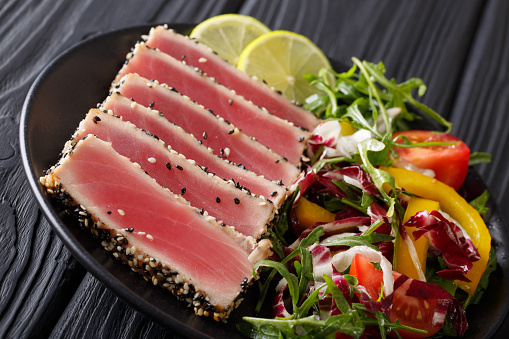 Delicious Tuna Steak in sesame, lime and salad of fresh vegetables and herbs close-up on a plate. horizontal