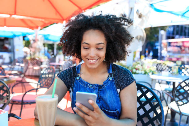 istock Smiling african woman drinking cocktail in cafeteria and using smart phone 1035963984