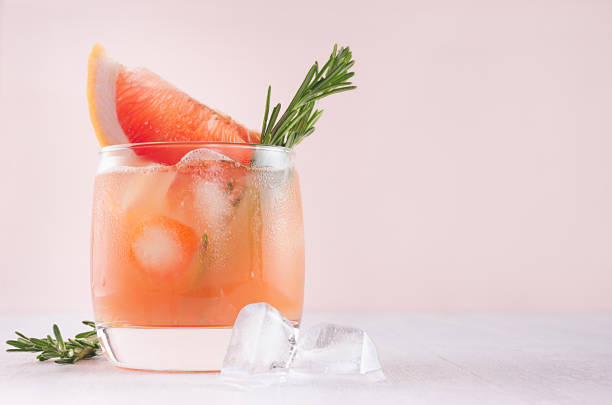 istock Cold grapefruit alcohol cocktail in misted glass with rosemary and grapefruits slice closeup on pastel fashion pink background. 1035978132