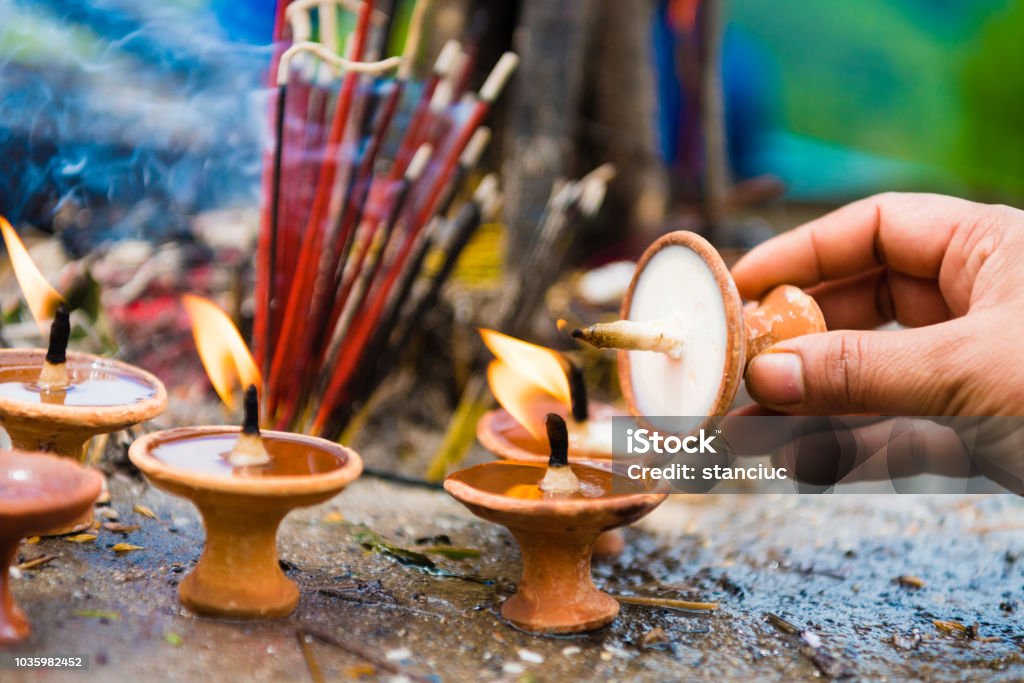 Woman hand with terra-cota oil lamps as religious offerings at temple in Nepal. Incence sticks over blurred background. Diwali Stock Photo