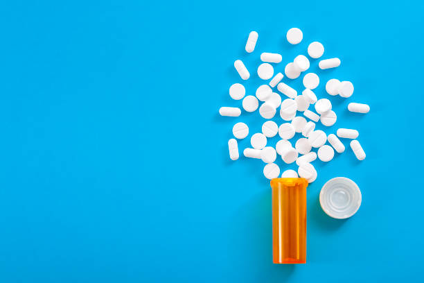 Pills falling from pill bottle on blue background with copyspace Medicine, opioid painkillers and prescription medicines concept with top view of orange prescription bottle of oxycodone and hydrocodone pills spilled on a blue background with copy space painkiller stock pictures, royalty-free photos & images