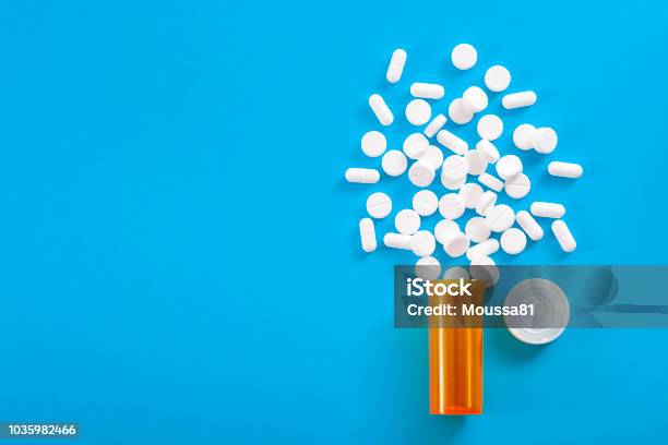 Pills Falling From Pill Bottle On Blue Background With Copyspace Stock Photo - Download Image Now