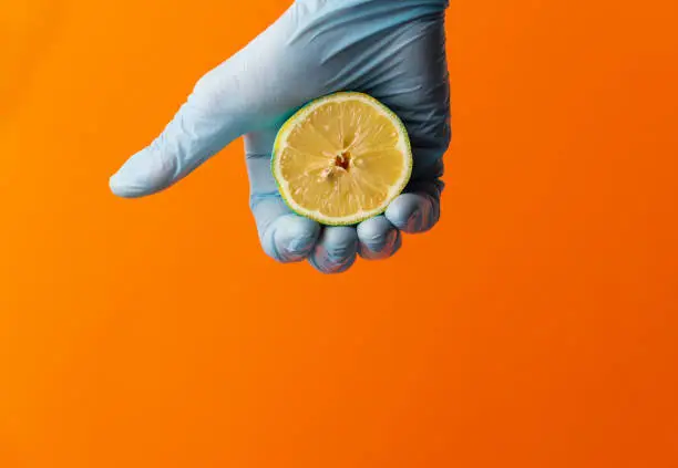 Hand in blue glove hold lemon on an orange background. Copy space