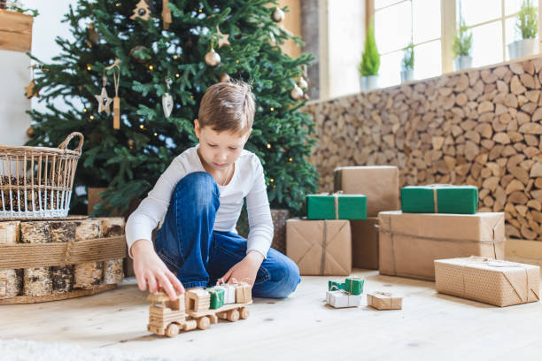 Boy playing toys unter christmas tree. Wooden car with small gifts. stock photo