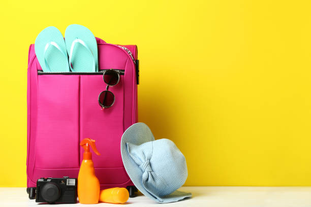 istock Pink suitcase with flip-flops, hat, sunglasses and sunscreen bottles on wooden table 1035984852