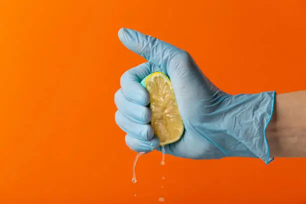 Hand in blue glove squeeze lemon on an orange background. Copy space. Close-up
