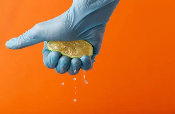 Hand in blue glove squeeze lemon on an orange background. Copy space