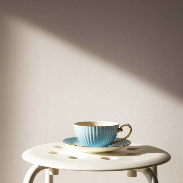 istock Blue vintage cup and saucer stands on a white stool against a white wall with shadow from the sun. Home cozy lifestyle 1036009154