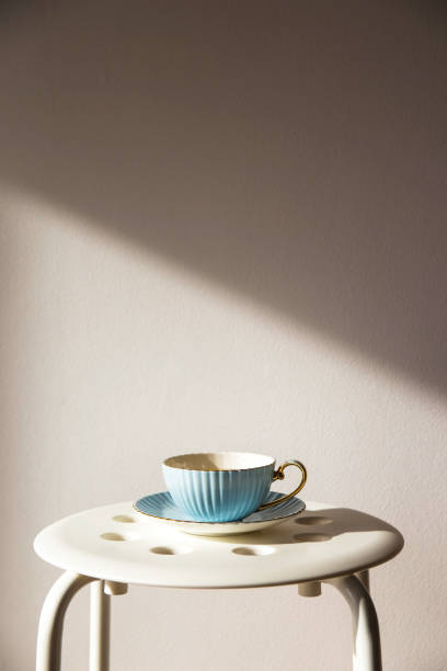 istock Blue vintage cup and saucer stands on a white stool against a white wall with shadow from the sun. Home cozy lifestyle 1036009158