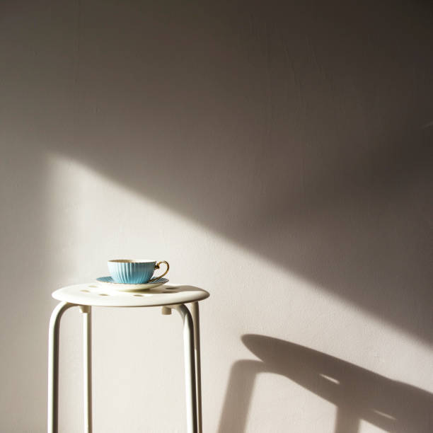 istock Blue vintage cup and saucer stands on a white stool against a white wall with shadow from the sun. Home cozy lifestyle 1036009184