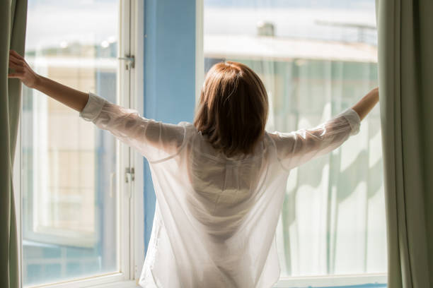 istock woman opening curtains 1036009314