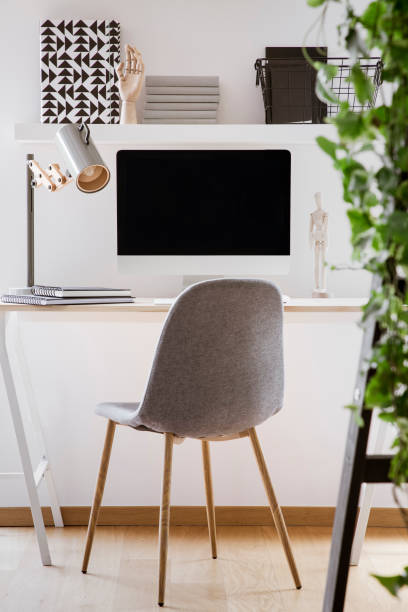 istock Grey chair at desk with desktop computer and lamp in modern white workspace interior. Real photo 1036026826