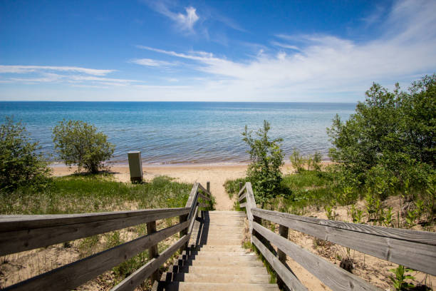 Stairs Lead To A Sunny Sandy Summer Beach On The Coast Of Great Lakes Waterfront park with a wide sandy beach on the shores of Lake Michigan in the downtown district of the Upper Peninsula city of Manistique Michigan. lake michigan stock pictures, royalty-free photos & images