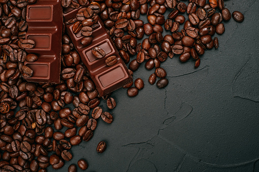 Roasted coffee beans and two bars of milk chocolate on the black concrete stone background. Flatlay style.